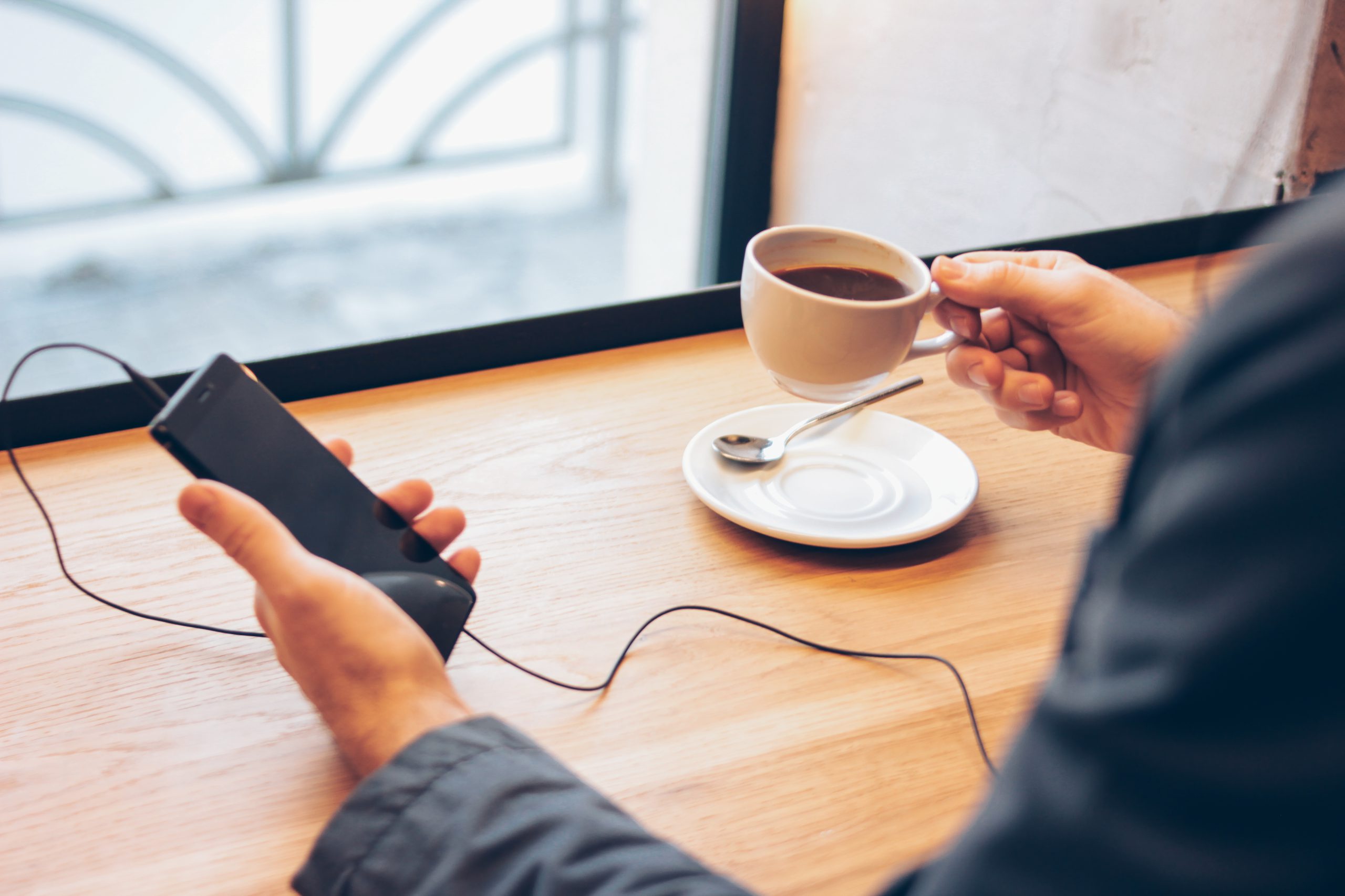 person looking at phone while drinking coffee, listening through headphones