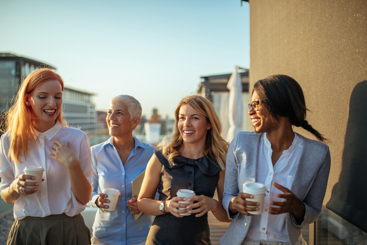 Photo of business women discussing about the project and drinking coffee on the rooftop.