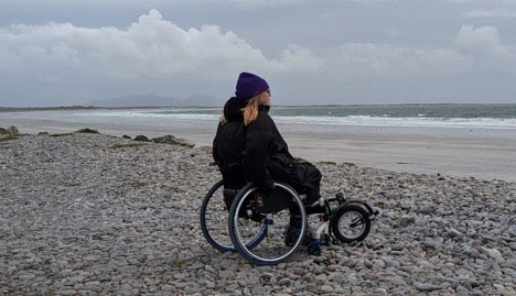 a women sitting in a wheelchair on a pebble beach