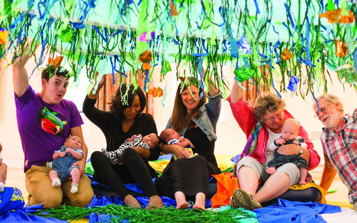 Adults holding babies play under green sea decorations